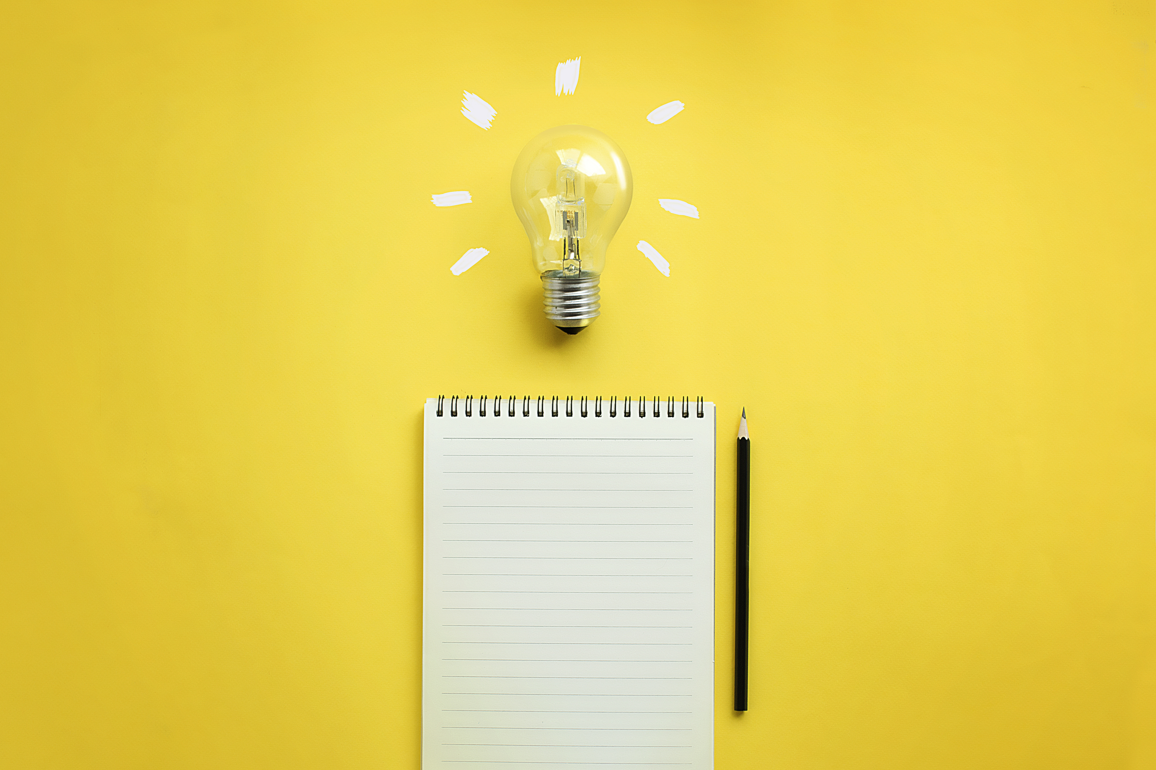 Lightbulb, notepad and pen on a yellow background