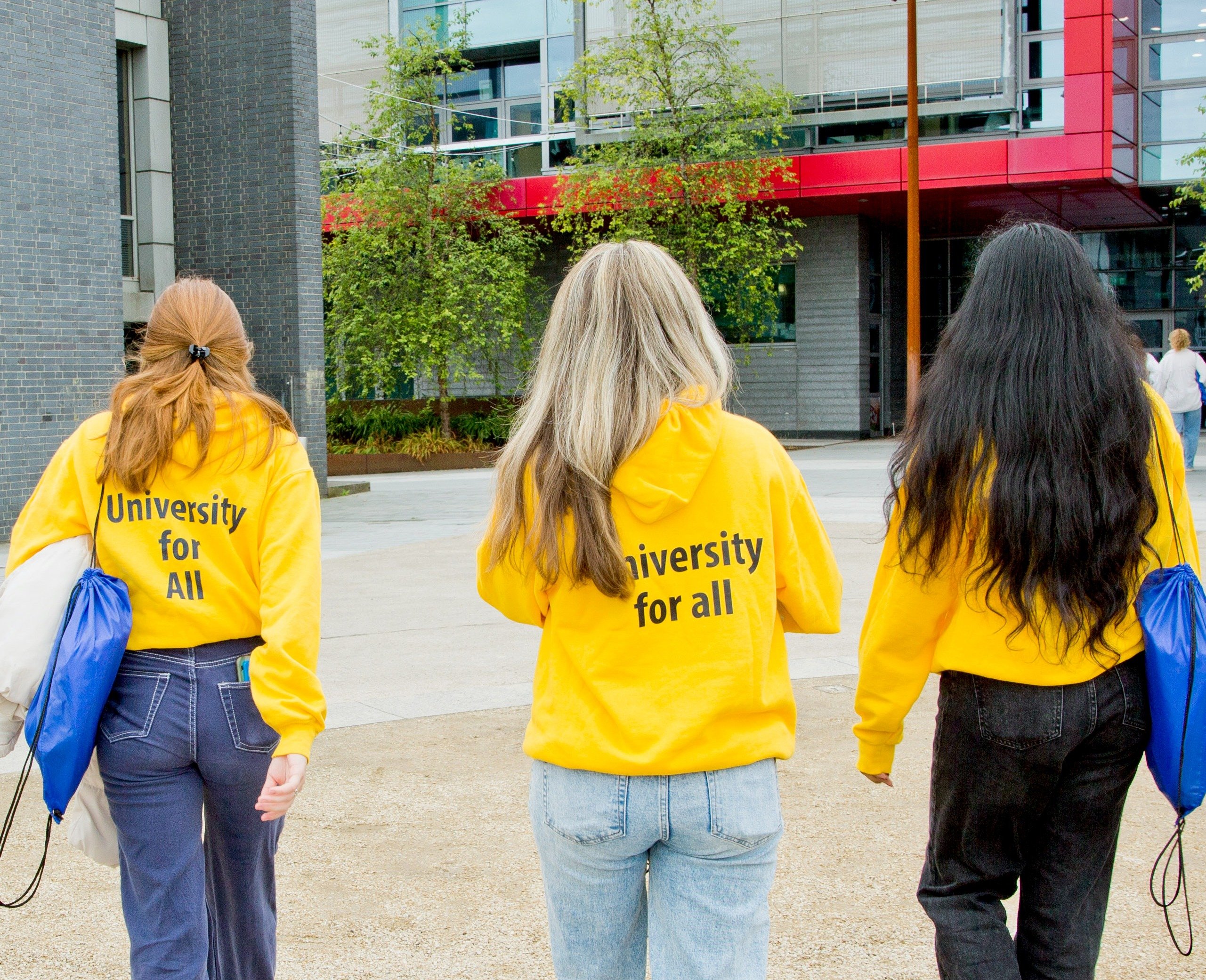 3 UCD students wearing university for all sweaters are walking on campus