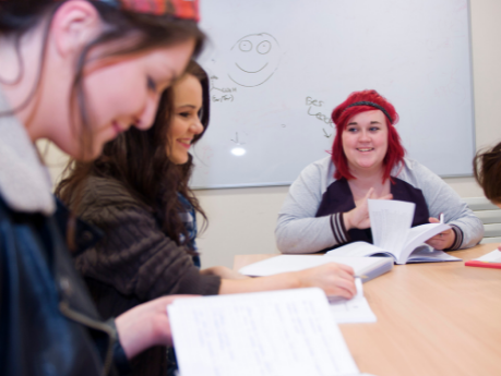 Students sit around a desk, smiling and laughing as they work together