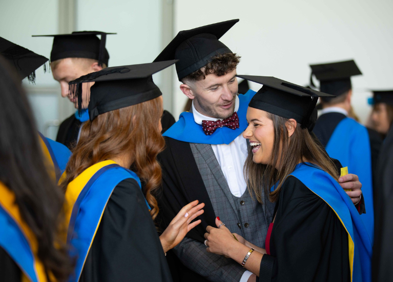 group of UCD alumni in graduation gowns and caps sharing a joyful moment.