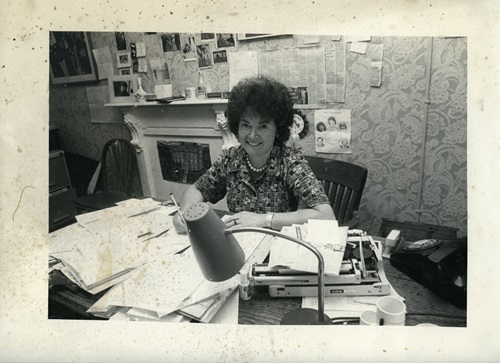 Black and white photograph of Gemma Hussey sitting behind desk covered with papers in constituency office