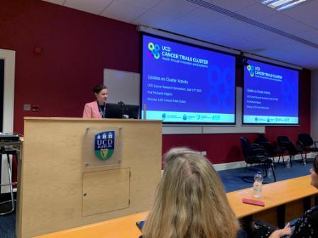 photograph of Prof Michaela higgins presenting at the UCD Cancer Symposium. She is standing at a lecturn in front of a projector.