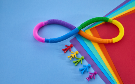 An image of a rainbow coloured infinity symbol on multicoloured pages with five small figurines in red, yellow, green, blue and purple.