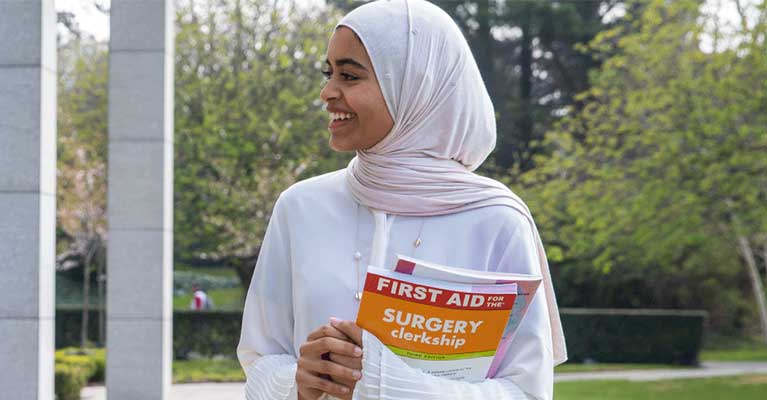 A female student walks by O'Reilly Hall as she hold first aid textbooks with both hands.