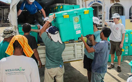 A group of humanitarian workers carry a large box from the back of a truck.