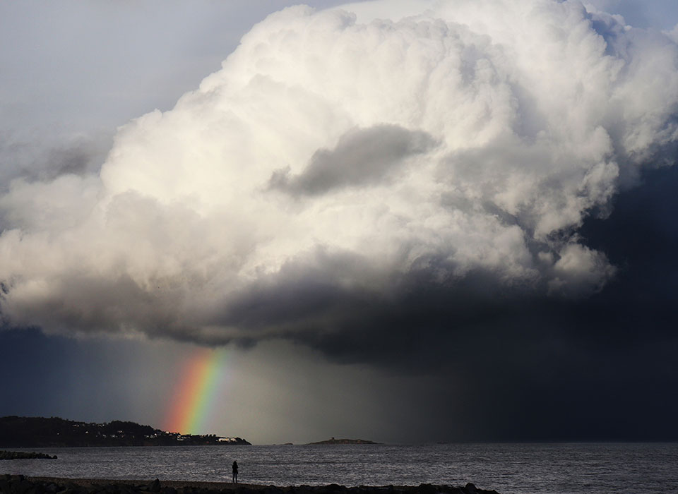 A giant cloud with a colourful rainbow shining on a peninsula.
