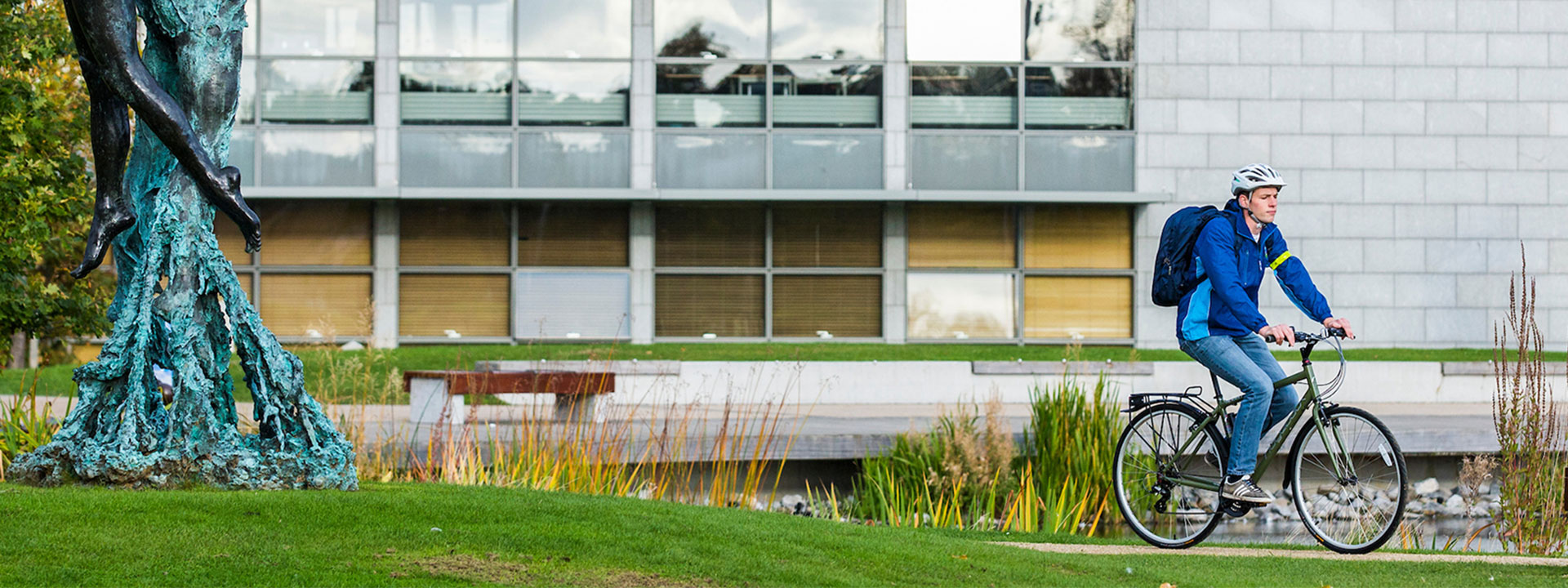 A student wearing a blue jacket and backpack cycles by the UCD upper lake.