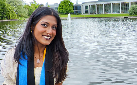 A UCD stands in front of the UCD lake smiling.