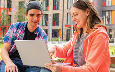 Two UCD students chat and laugh over a laptop on UCD campus.