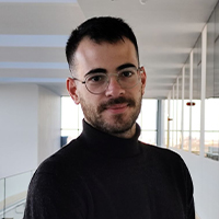 A young man with dark hair and glasses wears a black polo neck jumper.