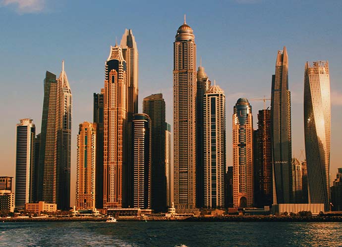Dubai Marina skyline at sunset, dense cluster of modern high-rise towers seen from across the water.
