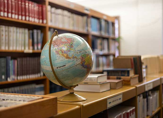 A globe on a library shelf surrounded by books, symbolizing global studies and international learning.