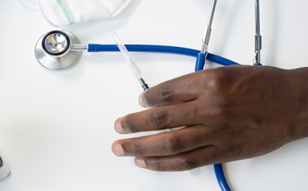 A person's hand holds a needle and a stethoscope.