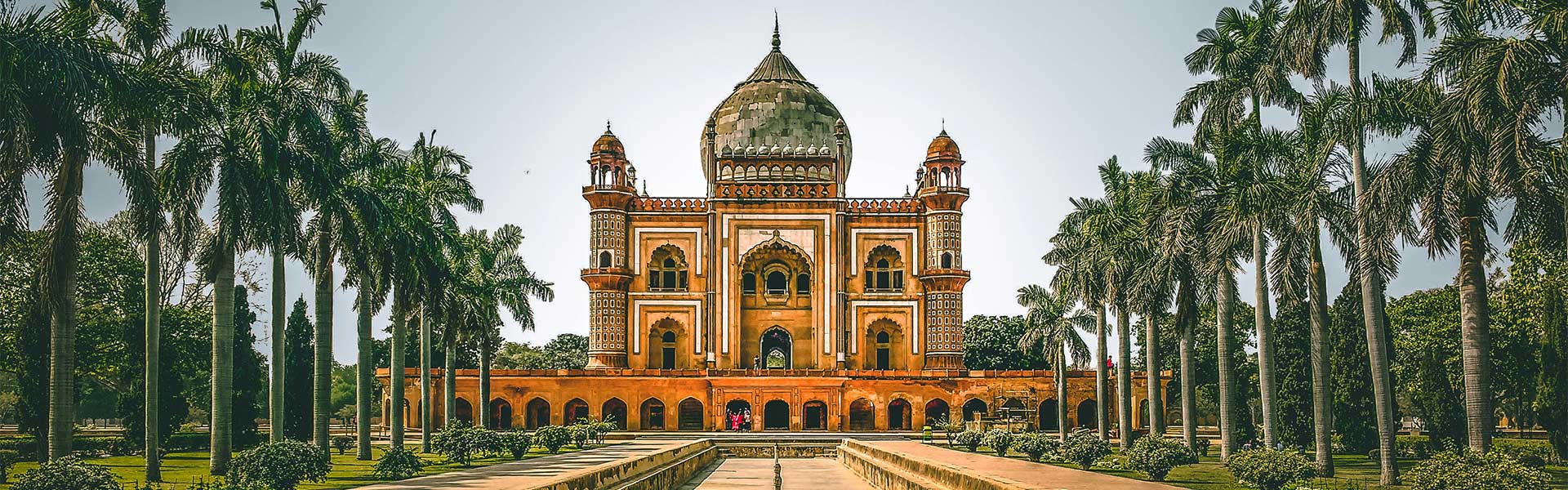Historic Mughal-style mausoleum with a large dome and arched entrances, surrounded by palm trees in a symmetrical garden setting.
