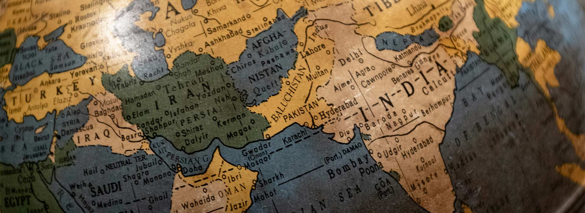 A close-up photograph of an old-style globe showing parts of the Middle East and South Asia, including Turkey, Iran, Afghanistan, Pakistan, and India. The map has muted vintage colors and slightly worn texture, with country names and major cities visible.