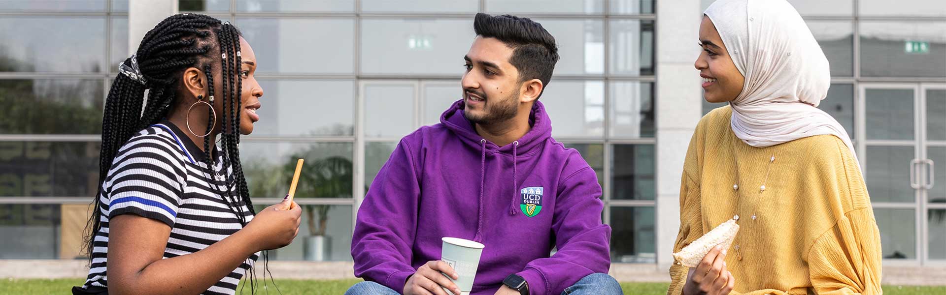 Three UCD students sitting outside, talking and eating together.