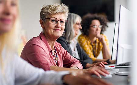 Group of women of different ages working at computers in a bright office setting.