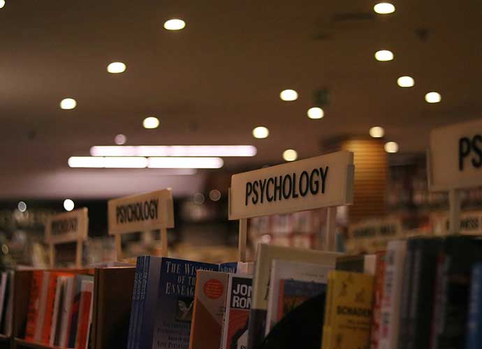 Bookshelves in a bookstore or library with section signs labeled “Psychology,” filled with books on the subject, under warm ceiling lights.