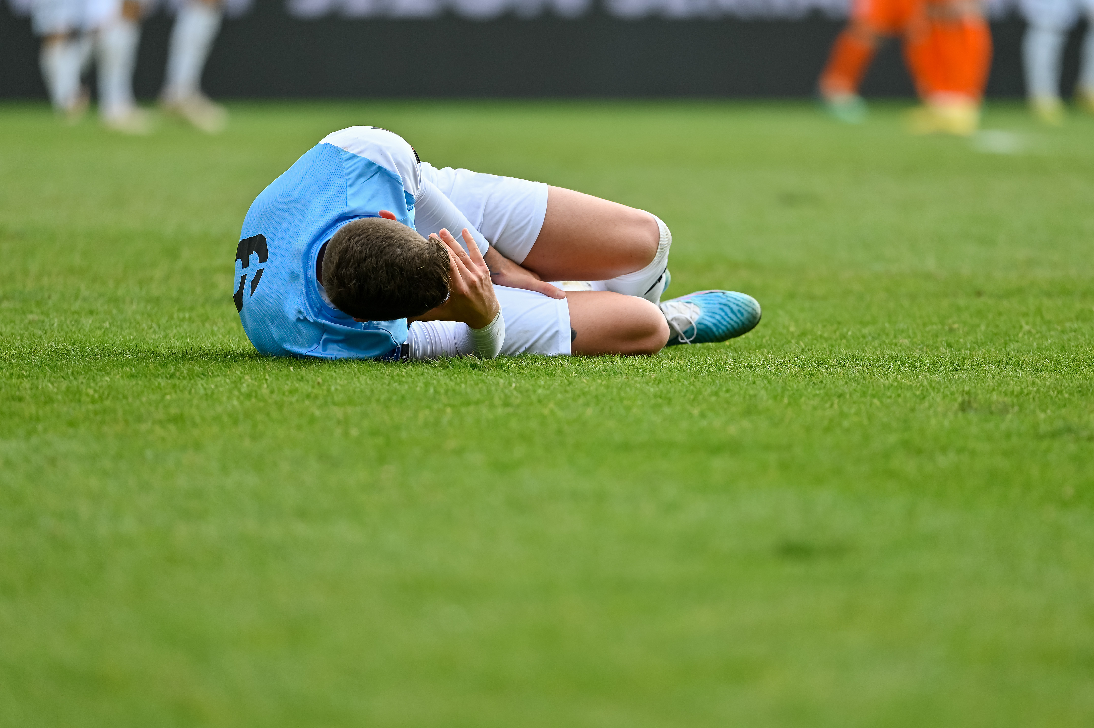 Young man lying on a pitch holding his head.