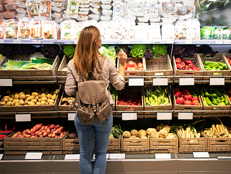 Good looking woman standing in front of vegetable shelves choosing what to buy. Buying groceries and healthy organic food in supermarket.