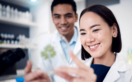 Male and female wearing white coats inspecting a petri dish