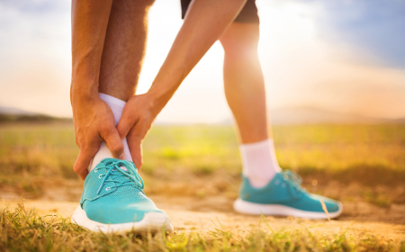 Male athlete wearing blue trainers holding his ankle