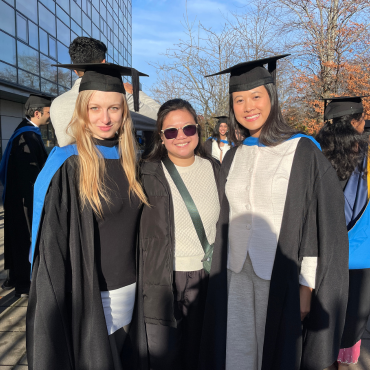 UCD graduates in caps and gowns outside on a sunny graduation day.