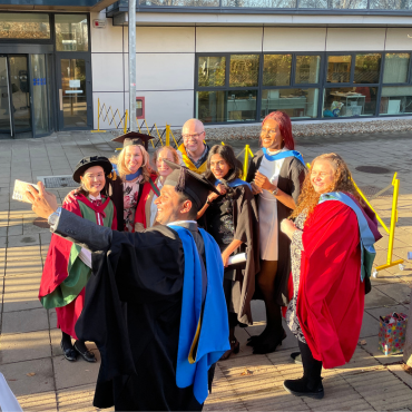 UCD graduates and UCD academic in caps and gowns outside on a sunny graduation day.