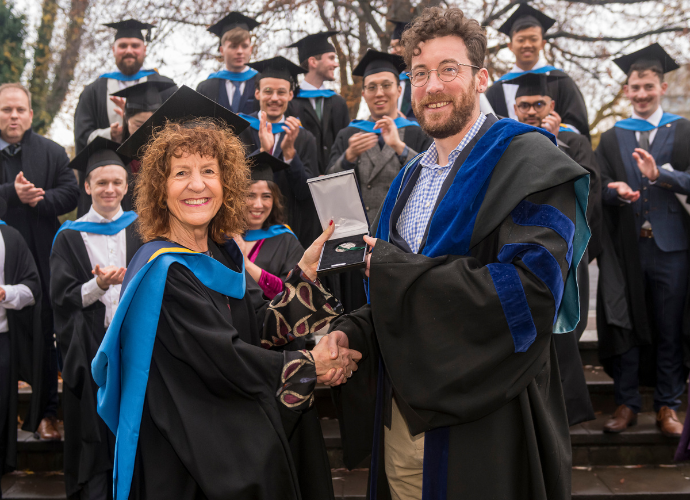 Female graduate in cap and gown receiving a medal from a male academic