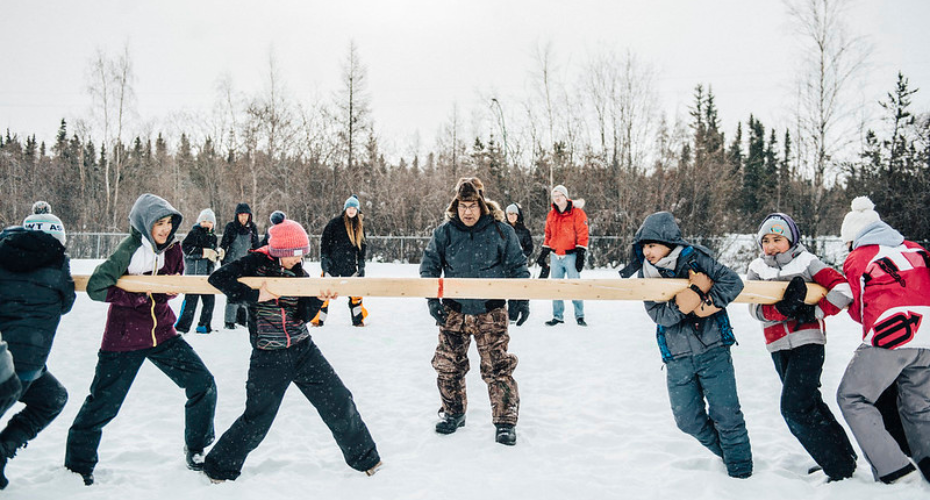 Children playing a tug of war game with a tree trunk in the snow