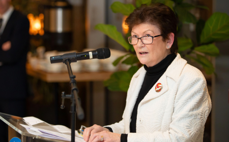 Woman with dark hair wearing a white jacket presenting at a podium