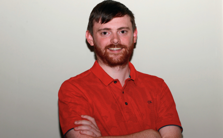 Dark haired man with a beard wearing a red top smiling to camera