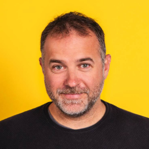 Image of a man with a beard wearing a black top against a yellow background