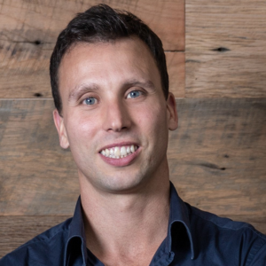 Man with dark hair and dark coloured shirt smiling to camera