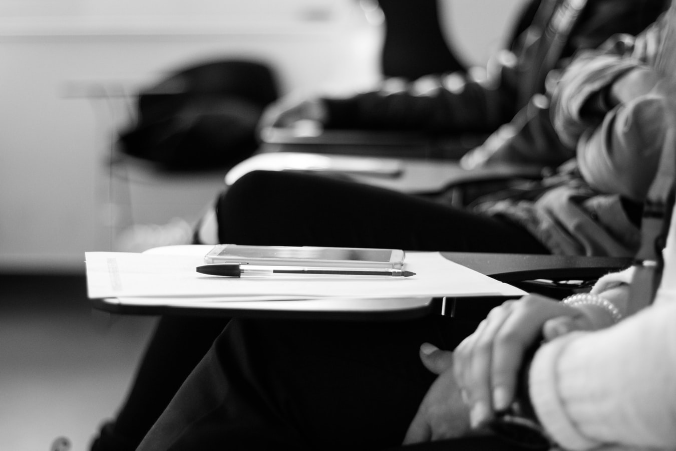 A black and white close up image of a students desk, pen and paper