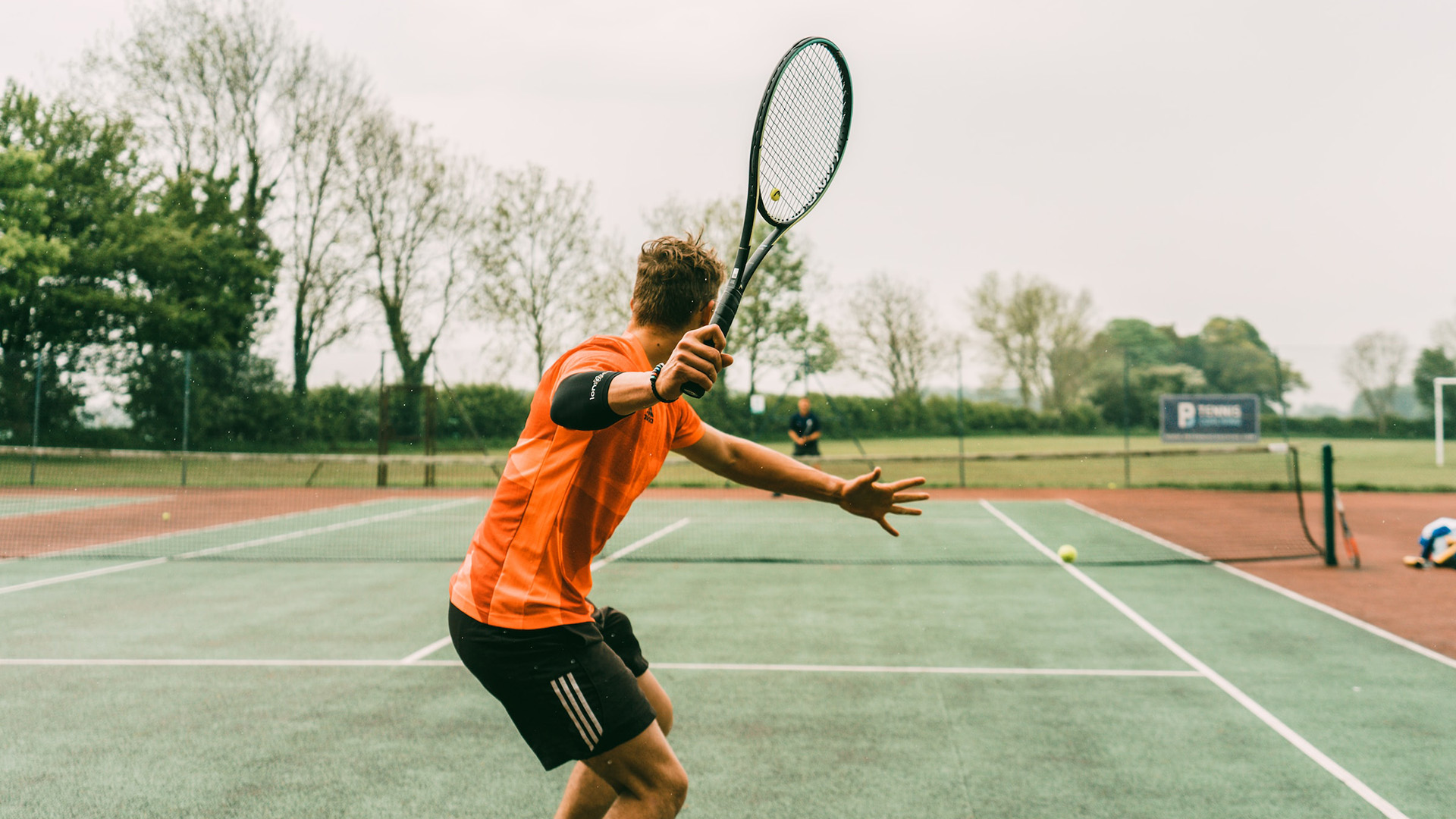 A man in an orange tee-shirt playing a tennis shot