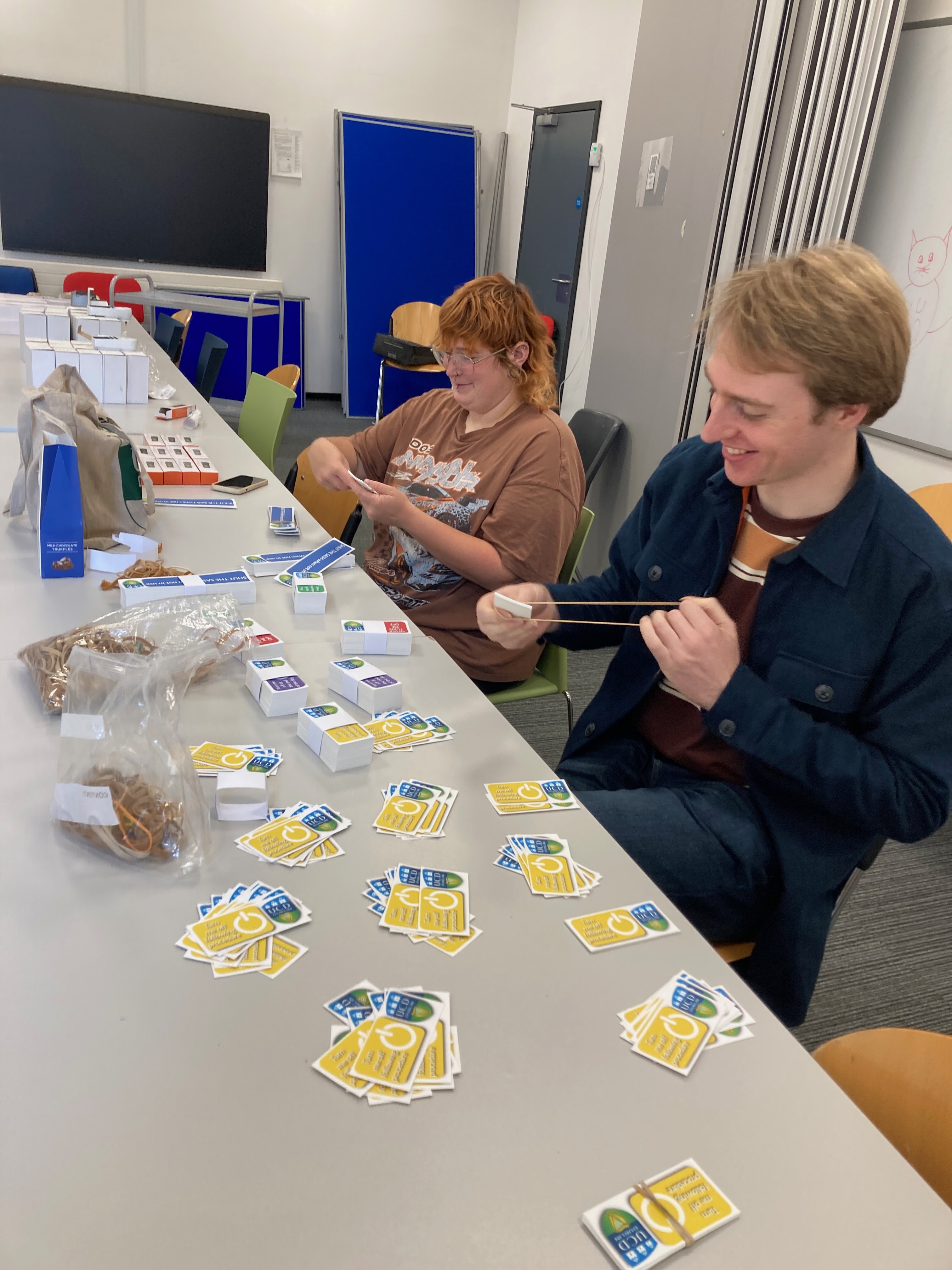 Two people sitting at a table making packets of stickers