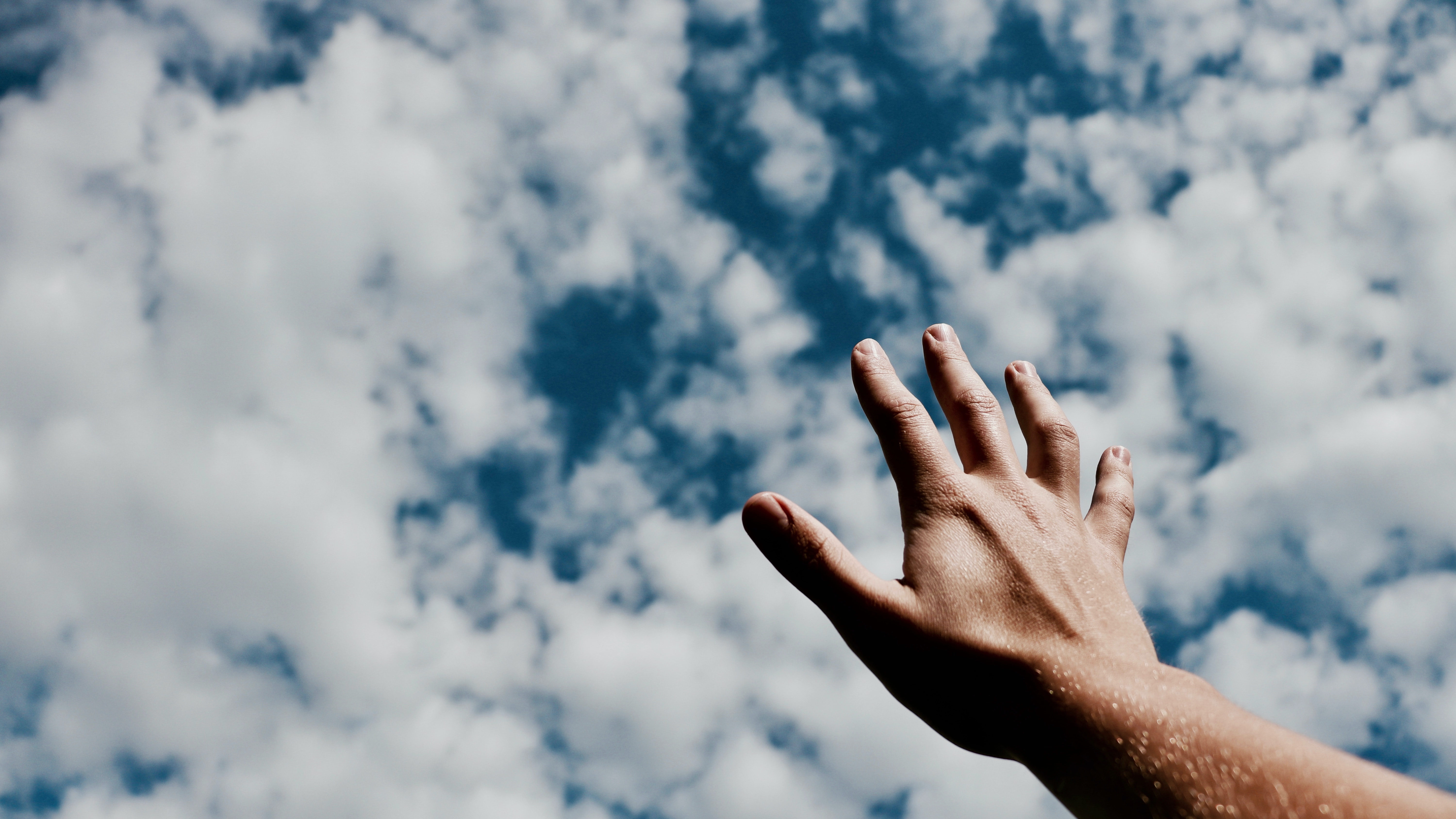 Hand reaching toward bright cloudy sky