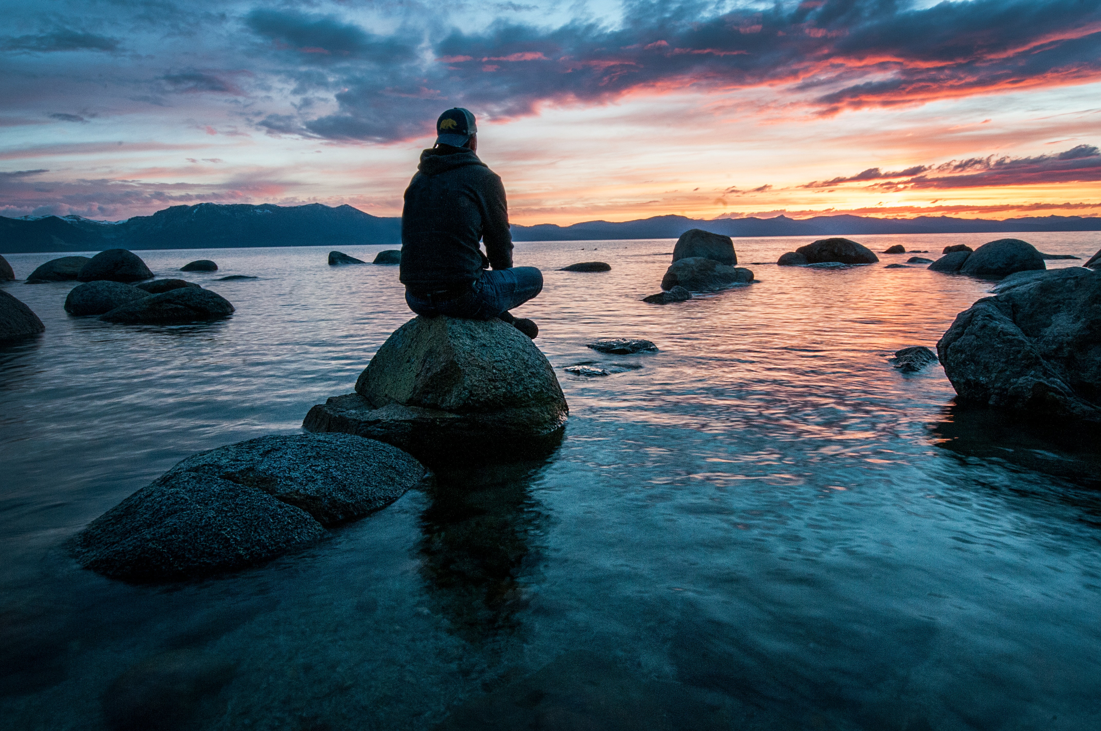 Man sitting on a rock, staring out to sea at sunset