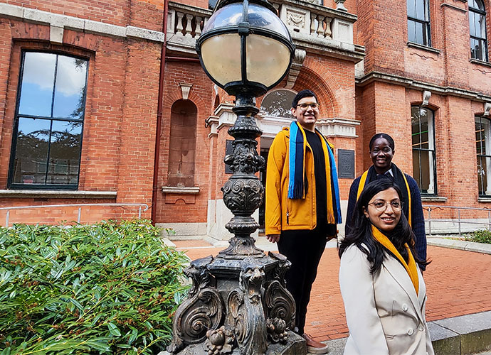 Tree students with UCD scarves stand in front of a red brick building.
