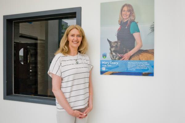 Mary Geary standing beside her Alumni Wall image